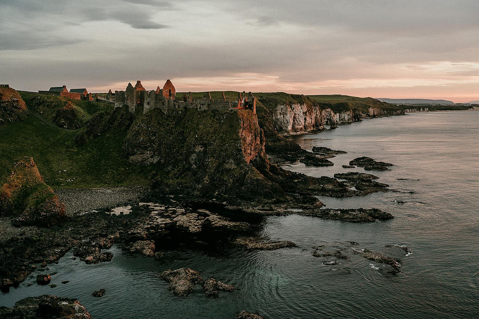 Dunluce Castle at dusk covered in the warm glow of the fading sun.