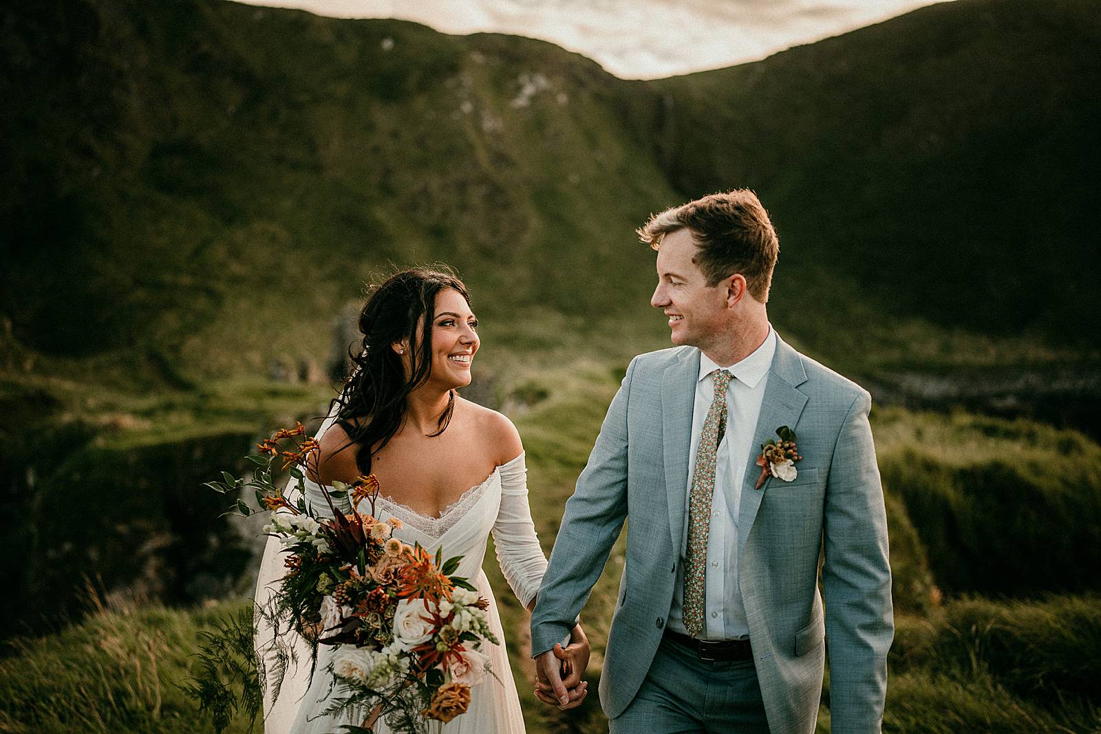 A happy bride and groom looking at each other as they walk through the irish landscape with Kinbane Castle in the background