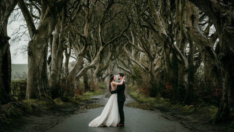 A couple embrace under the shelter of the canopy of trees at the Dark Hedges during a rain shower on their elopement day.