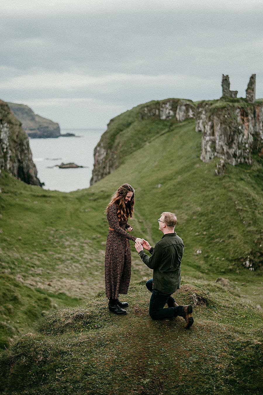 A guy down on one knee proposing to a girl at Dunseverick Castle in Northern Ireland.