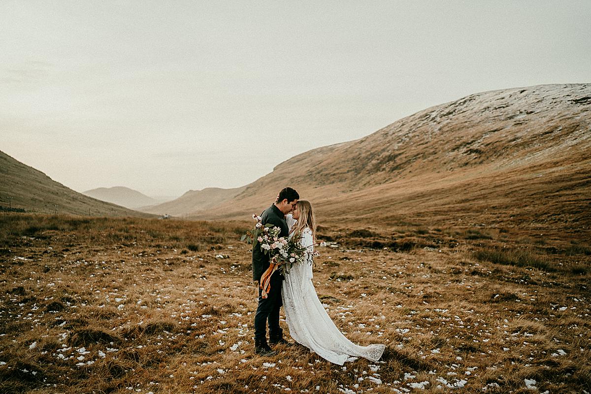 a bride in a boho wedding dress holding a large bouquet of flowers with her husband during a honeymoon session in the Mourne Mountains.